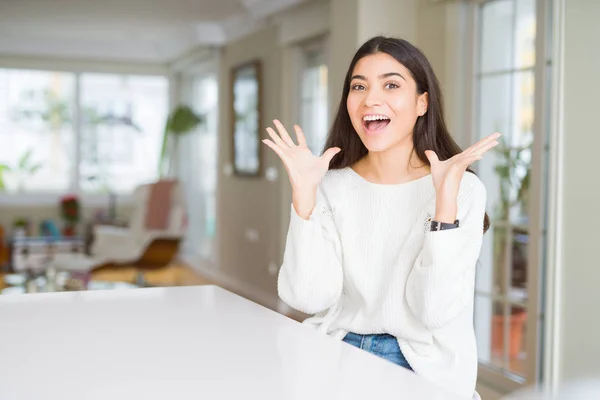 年轻的美女在家里的白色桌子上庆祝疯狂和惊讶的成功与手臂抬起和睁开眼睛尖叫兴奋 优胜者概念 — 图库照片