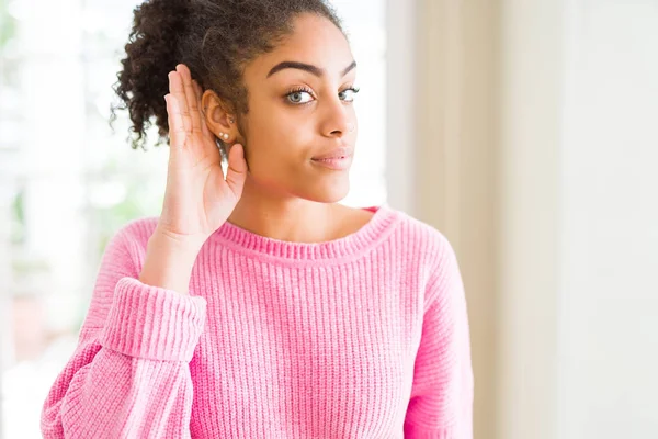 Beautiful young african american woman with afro hair smiling with hand over ear listening an hearing to rumor or gossip. Deafness concept.