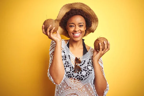Young african american woman with afro hair holding coconut over yellow isolated background with a happy face standing and smiling with a confident smile showing teeth