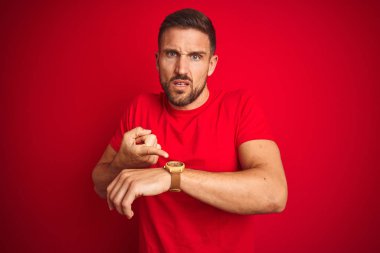 Genç yakışıklı adam kırmızı izole arka plan üzerinde rahat t-shirt giyen acele zaman izlemek için işaret, sabırsızlık, üzgün ve son gecikme için kızgın