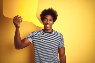 Genç afro-amerikan adam mutlu bir yüz ayakta ve dişleri gösteren kendinden emin bir gülümseme ile gülümseyerek izole sarı arka plan üzerinde duran konuşma balonu tutan