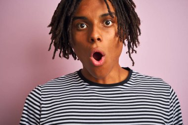 Afro amerikan adam dreadlocks giyen lacivert çizgili t-shirt izole pembe arka plan üzerinde sürpriz bir yüz ile şok korkmuş, korku ve korku ifade ile heyecanlı