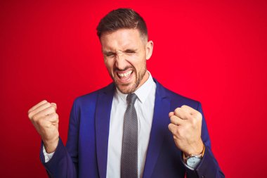 Kırmızı izole arka plan üzerinde genç yakışıklı iş adamı çok mutlu ve heyecanlı kolları kaldırdı ile kazanan jest yapıyor, gülümseyerek ve başarı için çığlık. Kutlama konsepti.