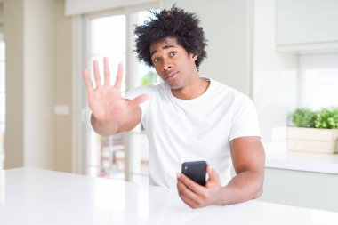 Afrika kökenli Amerikalı adam açık eliyle dur işareti ile ciddi ve kendine güvenen ifade, savunma jest yapıyor Smartphone kullanarak