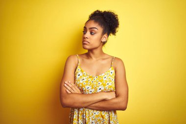 Izole sarı arka plan üzerinde duran rahat çiçekli elbise giyen Afro-amerikan kadın kolları ile yan bakarak ikna ve kendinden emin geçti