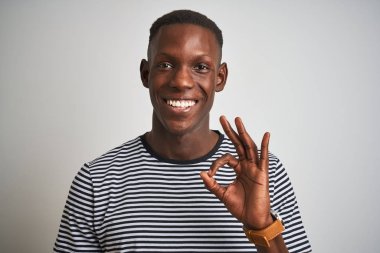 Izole beyaz arka plan üzerinde duran lacivert çizgili t-shirt giyen Afro-Amerikan adam parmakları ile ok işareti yapıyor, mükemmel sembolü