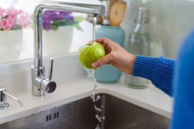 Genç kadın lavabo su kullanarak sebze ve meyve yıkama