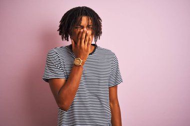 Dreadlocks lacivert çizgili t-shirt izole pembe arka plan üzerinde duran dreadlocks giyen afro adam bir şey kokulu ve, dayanılmaz koku kokuyor, burun parmakları ile nefes tutarak. Kötü kokular kavramı.