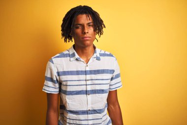 Izole sarı arka plan şüpheci ve sinir üzerinde çizgili gömlek giyen dreadlocks ile Afro Amerikan adam, sorun nedeniyle üzgün kaşlarını çatma. Negatif kişi.