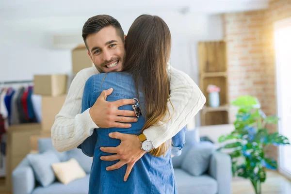 Junges Paar zieht in ein neues Zuhause, umarmt sich verliebt und zeigt Schlüssel — Stockfoto