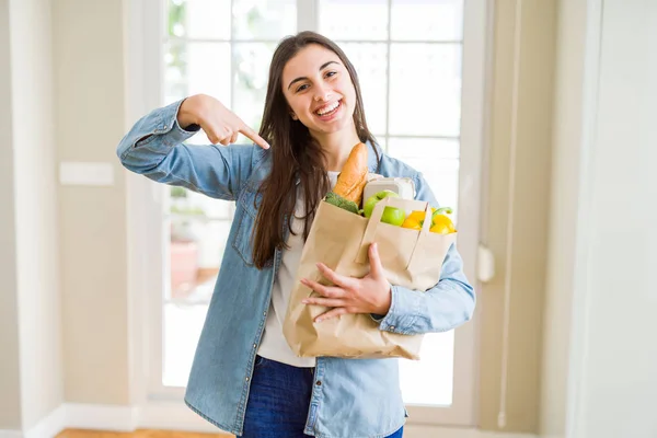 健康的な食料品でいっぱいの紙袋を持つ美しい若い女性は 驚きの顔が自分自身に指を指さす — ストック写真