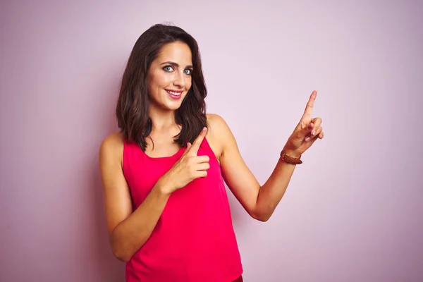 年轻的漂亮女人穿着T恤站在粉红色孤立的背景微笑 看着相机指着两只手和手指的一侧 — 图库照片
