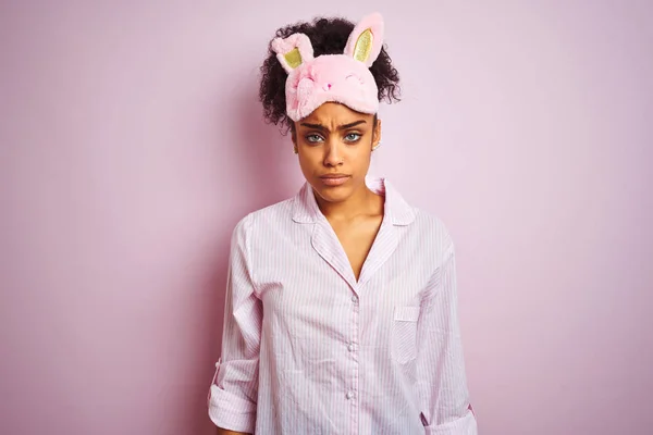 孤立したピンクの背景にパジャマとマスクを着けた若いアフリカ系アメリカ人女性は懐疑的で神経質で 問題のために動揺して顔をしかめた 否定的な人 — ストック写真