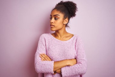 Genç afro-amerikan kadın kollarını ile yan bakarak izole pembe arka plan üzerinde duran kış kazak giyen ikna ve kendinden emin geçti