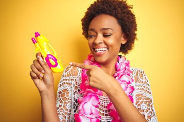Afro saçlı genç afro-amerikalı kadın çiçek hawaiian lei ve su tabancası giyen çok mutlu el ve parmak ile işaret