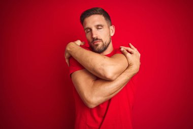 Genç yakışıklı adam kırmızı izole arka plan üzerinde rahat t-shirt giyen kendini mutlu ve olumlu sarılma, kendinden emin gülümseyen. Öz sevgi ve öz bakım