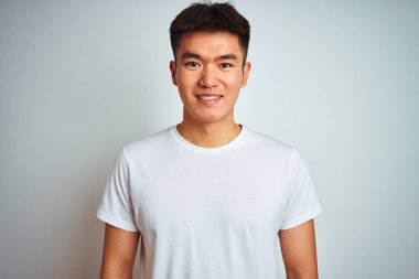 Genç Asyalı Çinli adam yüzünde mutlu ve serin bir gülümseme ile izole beyaz arka plan üzerinde duran t-shirt giyiyor. Şanslı kişi.
