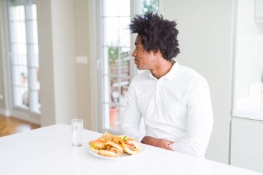 Afro-Amerikan aç adam yan bakarak öğle yemeği için hamburger yeme, kendine güvenen gülümseme ile doğal yüzü ile profil poz rahatlayın.