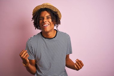 Izole pembe arka plan üzerinde lacivert t-shirt ve şapka giyen dreadlocks ile Afro Amerikan adam çok mutlu ve heyecanlı silah kaldırdı ile kazanan jest yapıyor, gülümseyen ve başarı için çığlık. Kutlama konsepti.