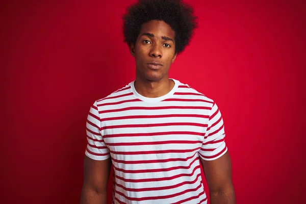 年轻的非洲裔美国男子穿着条纹T恤在孤立的红色背景放松与严肃的表情的脸 简单自然地看着相机 — 图库照片