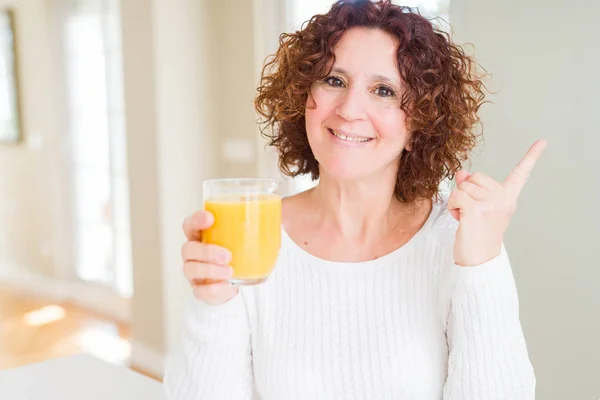 高级妇女抚摸着一杯新鲜的橙汁 很高兴用手和手指指着一边 — 图库照片