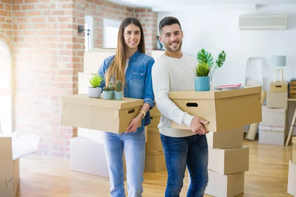 Pareja joven mudándose a un nuevo hogar, sonriendo feliz sosteniendo cardboa —  Fotos de Stock