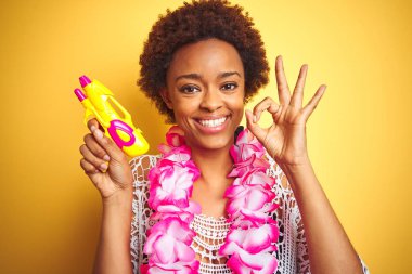 Afro saç giyen çiçek Hawaiian Lei ve su tabancası ile genç Afrikalı Amerikan kadın parmaklar ile ok işareti yapıyor, mükemmel sembolü
