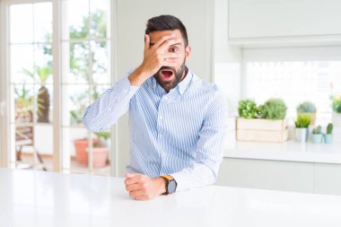 Yakışıklı İspanyol iş adamı şok el ile yüz ve gözleri kapsayan gözetleme, utanmış ifade ile parmaklarından bakarak.