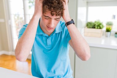 Genç yakışıklı adam giyiyor rahat mavi t-shirt ev umutsuz ve stresli baş ağrısı çünkü acı, ağrı ve Migren. Ellerini kafasına.