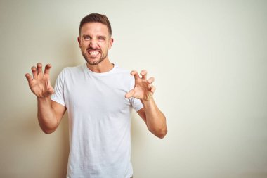 Genç yakışıklı adam izole arka plan üzerinde rahat beyaz t-shirt giyen kedi, agresif ve seksi ifade olarak pençe jest yapıyor komik gülümseyerek