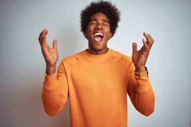Afro saçlı, izole beyaz arka plan üzerinde turuncu kazak giyen genç Amerikalı adam kollarını kaldırdı ve kapalı gözleri heyecan çığlık ile başarı için deli ve deli kutluyor. Kazanan kavramı