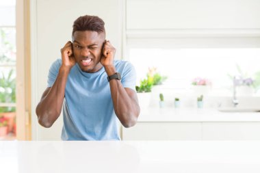 Yakışıklı afro-amerikan adam evde rahat t-shirt giyen yüksek sesle müzik sesi için rahatsız ifade ile parmakları ile kulakları kapsayan. Sağır kavramı.