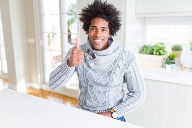 Kış lık kazak giyen Afro-Amerikan adam eliyle jest yaparak mutlu başparmaklar yapıyor. Başarı göstererek kameraya bakan ifadeyi onaylama.