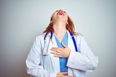 Genç kızıl saçlı doktor kadın beyaz izole arka plan üzerinde stetoskop kullanarak size gülüyor, vücut üzerinde el ile kameraya parmak işaret, utanç ifade