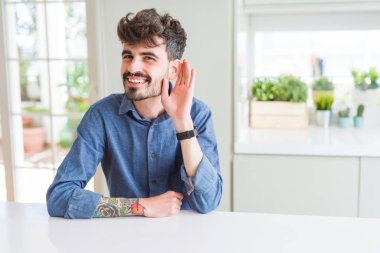 Beyaz masanın üzerinde oturan rahat gömlek giyen genç adam, söylenti ya da dedikodu ları dinlerken eliyle gülümseyerek kulaktan kulağa gülümsüyor. Sağırlık kavramı.