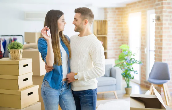 Casal jovem se mudando para uma nova casa, abraçando no amor mostrando chaves — Fotografia de Stock