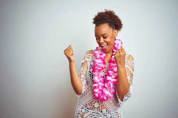 Young african american woman with afro hair wearing flower hawaiian lei over isolated background very happy and excited doing winner gesture with arms raised, smiling and screaming for success. Celebration concept.