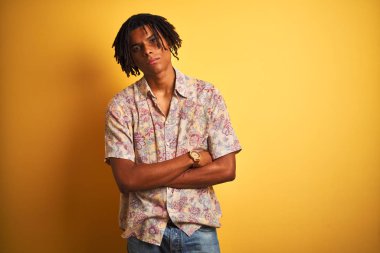 Izole sarı arka plan şüpheci ve sinir üzerinde çiçek gömlek giyen tatilde dreadlocks ile Afro adam, çapraz kolları ile yüzünde ifade onaylamayan. Negatif kişi.