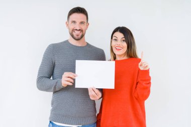 Genç çift izole arka plan üzerinde boş yapraklık kağıt tutan bir fikir veya soru mutlu yüz, bir numara ile parmak işaret ile şaşırttı