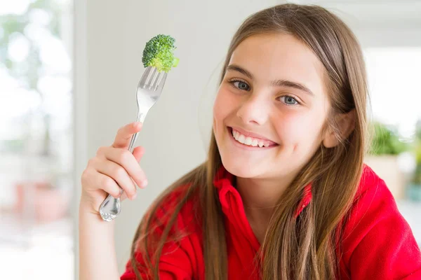 歯を見せる自信に満ちた笑顔で立ち上がり 笑顔で新鮮なブロッコリーを食べる美しい若い女の子 — ストック写真
