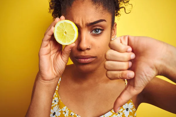 若いアフリカ系アメリカ人女性は 怒った顔で孤立した黄色の背景の上にレモンのスライスを保持し 親指を下に嫌いを示す否定的な兆候 拒絶概念 — ストック写真