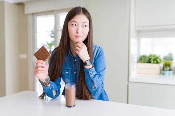 美しいアジアの女性がチョコレートミルクセーキを飲み チョコレートバーを持つ真剣な顔は質問を考え 非常に混乱したアイデア — ストック写真