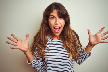 Genç güzel kadın beyaz izole arka plan üzerinde çizgili t-shirt giyen deli kutluyor ve kollarını kaldırdı ve açık gözleri heyecanlı çığlık ile başarı için hayran. Kazanan kavramı