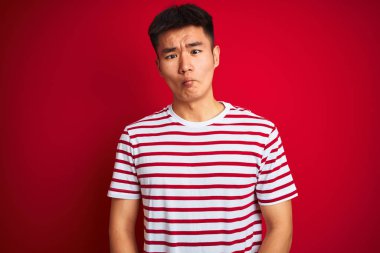 Genç Asyalı Çinli adam çizgili t-shirt dudaklar, deli ve komik jest ile balık yüz yapma izole kırmızı arka plan üzerinde duran giyiyor. Komik ifade.