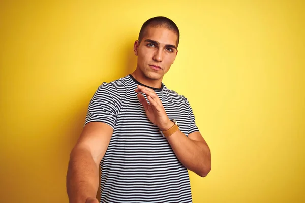 Young handsome man wearing striped t-shirt over yellow isolated background disgusted expression, displeased and fearful doing disgust face because aversion reaction. With hands raised. Annoying concept.