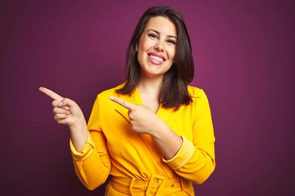 Young beautiful brunette woman wearing elegant yellow jacket over purple isolated background smiling and looking at the camera pointing with two hands and fingers to the side.