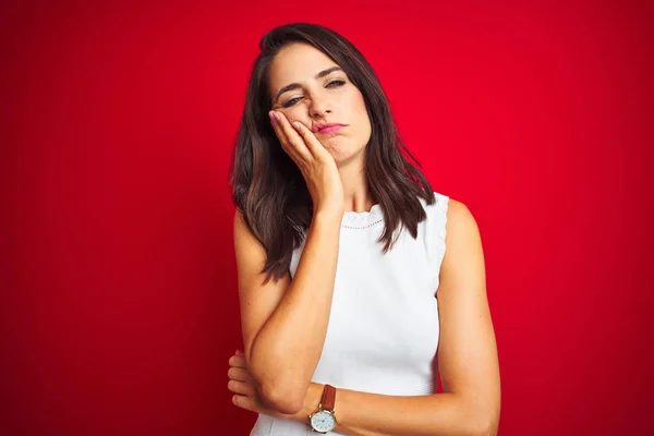 Young beautiful woman wearing white dress standing over red isolated background thinking looking tired and bored with depression problems with crossed arms.
