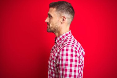 Kırmızı izole arka plan üzerinde genç yakışıklı adam yan bakıyor, doğal yüz ve kendine güvenen gülümseme ile profil poz dinlenmek.