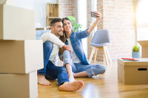 Jovem casal sentado no chão da nova casa tomando uma selfie p — Fotografia de Stock