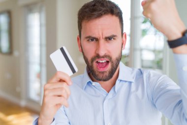 Yakışıklı iş adamı holding kredi kartı ile öfke, çılgın ve yükseltilmiş eliyle diye bağıran rahatsız ve hayal kırıklığına uğramış öfke kavramı bağırarak